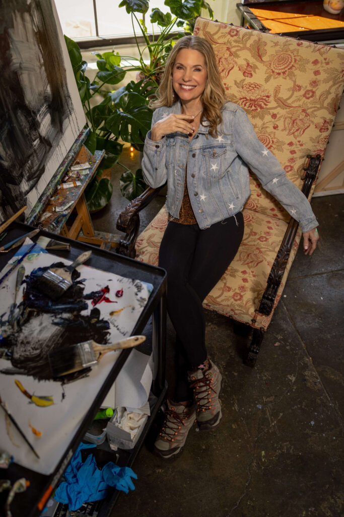 overhead shot of blonde woman sitting in a vintage chair with paint tubes and brushes