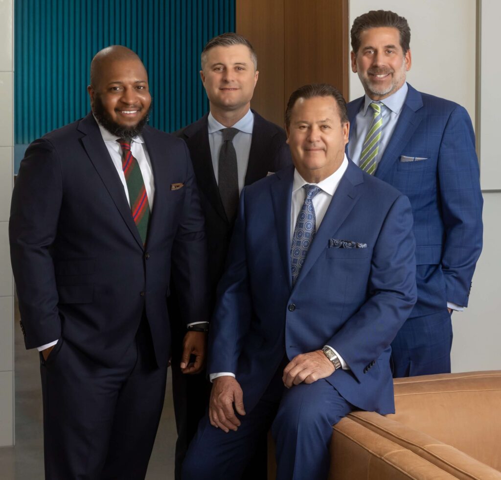 four men in stylish suits posing together against a teal and brown background