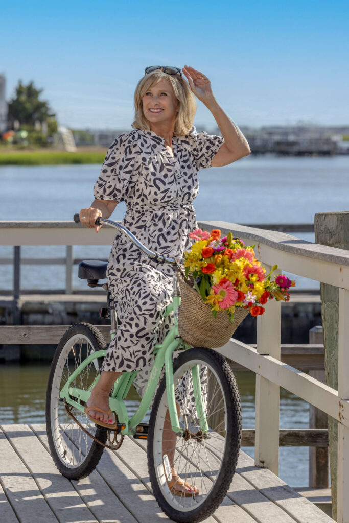 blonde woman riding a green bicycle by the bayside and reaching for sunglasses on her head at an editorial photo shoot in philadelphia
