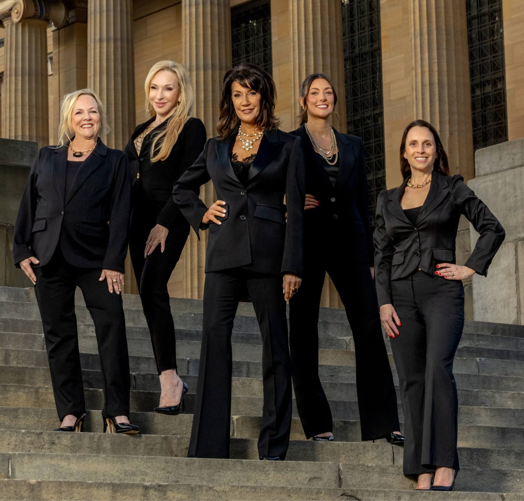 women posing in black suits in front of terracotta columns at golden hour