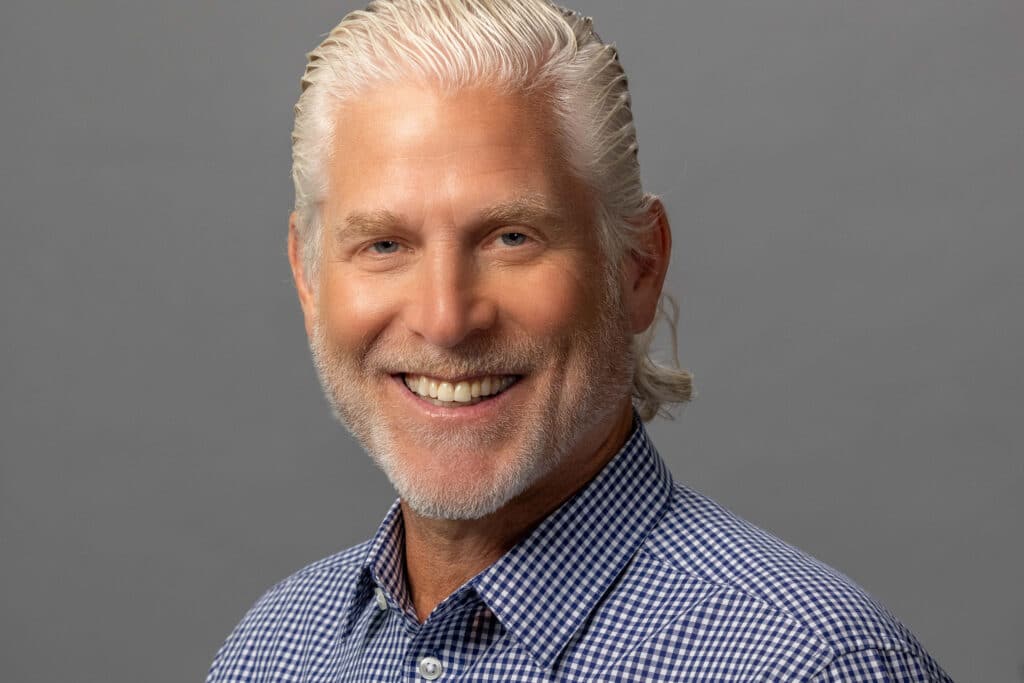 business professional man smiling in collared shirt against light gray background