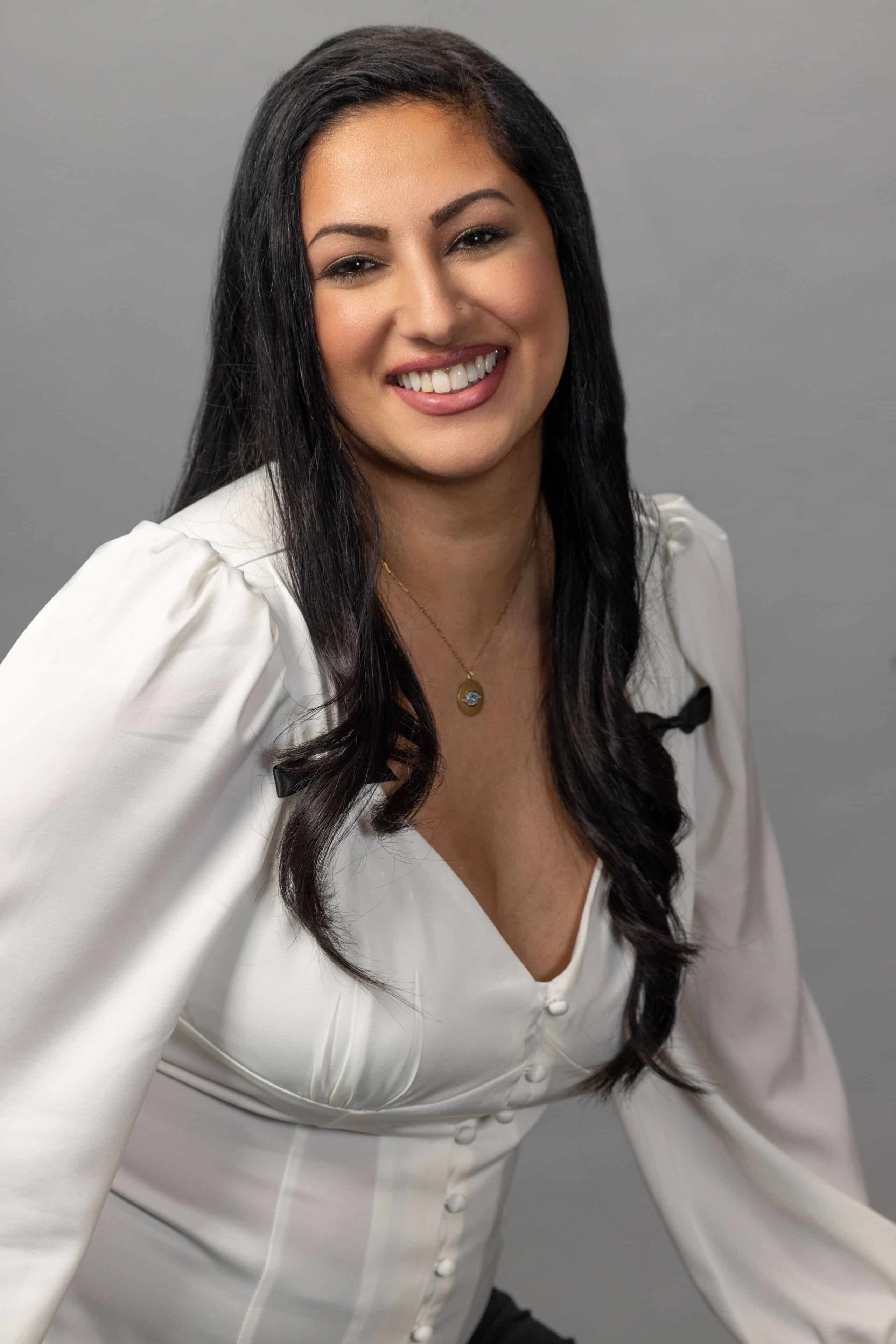 corporate business woman wearing a white shirt and smiling against a light gray background