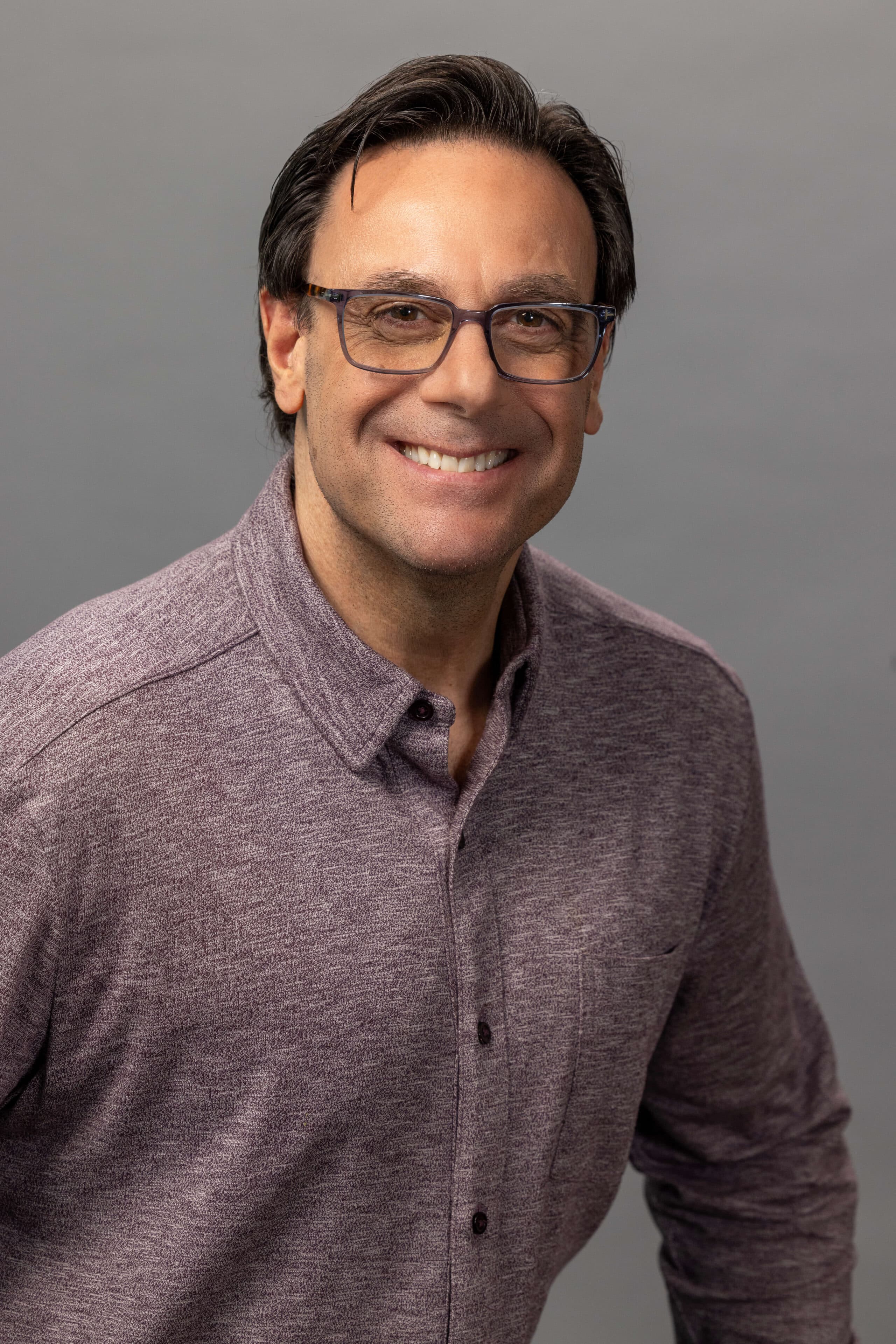 business man wearing a red collared shirt and smiling against a gray background