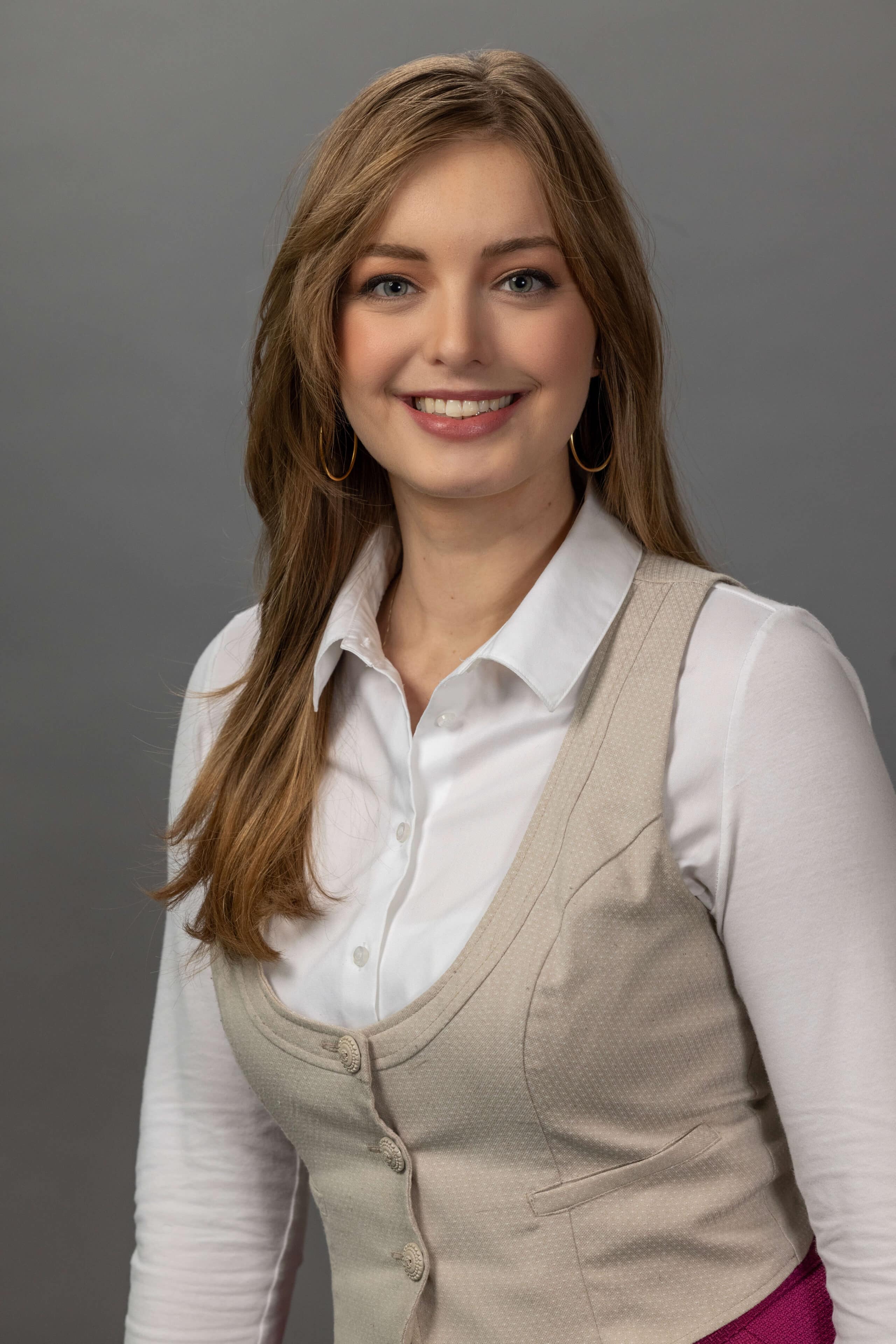 business professional woman in a beige vest and collared shirt posing for headshot against gray background