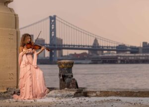 woman in pink dress playing the violin with blue bridge in background