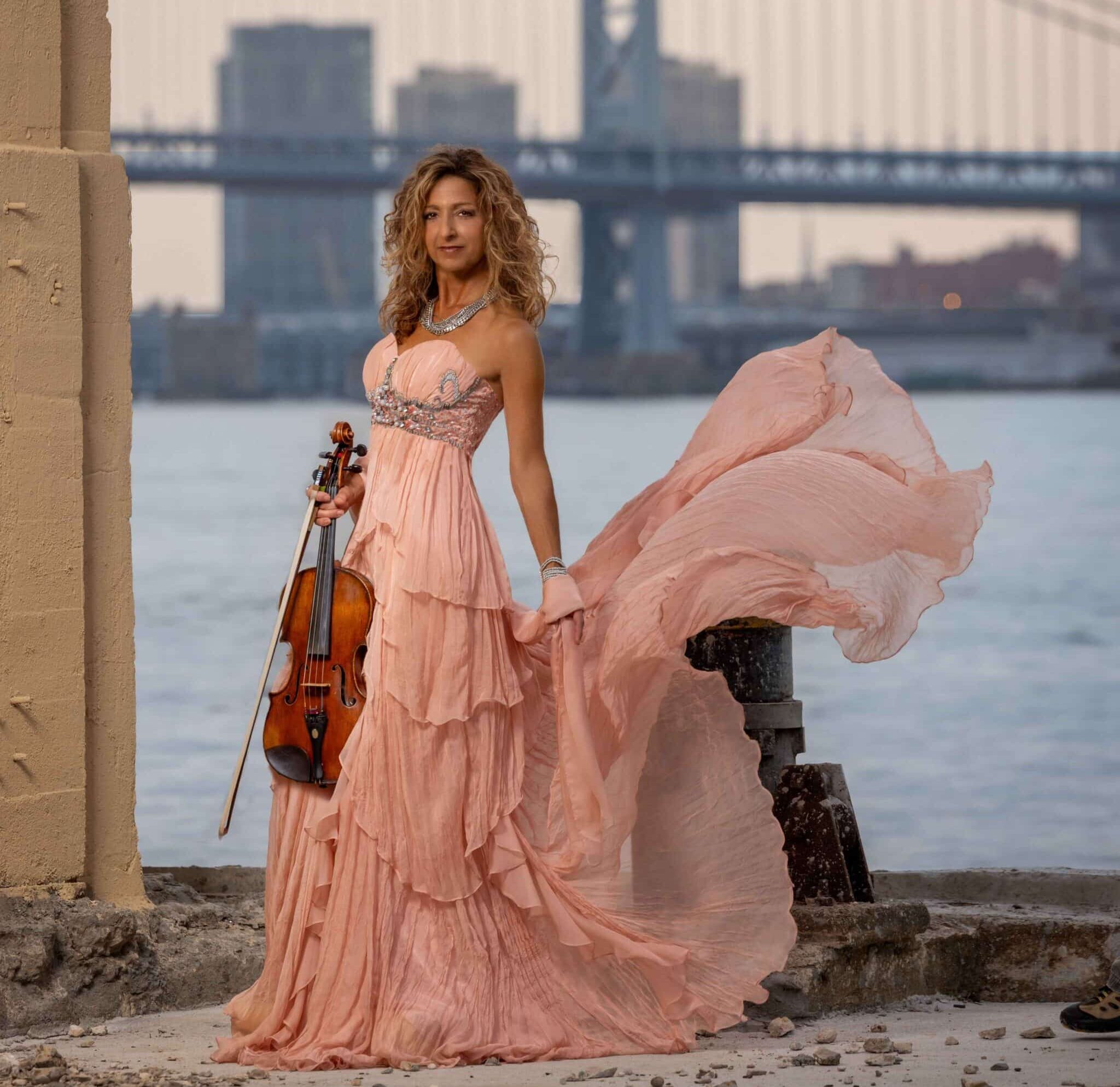 woman wearing a pink dress and holding a violin in an outdoor industrial setting