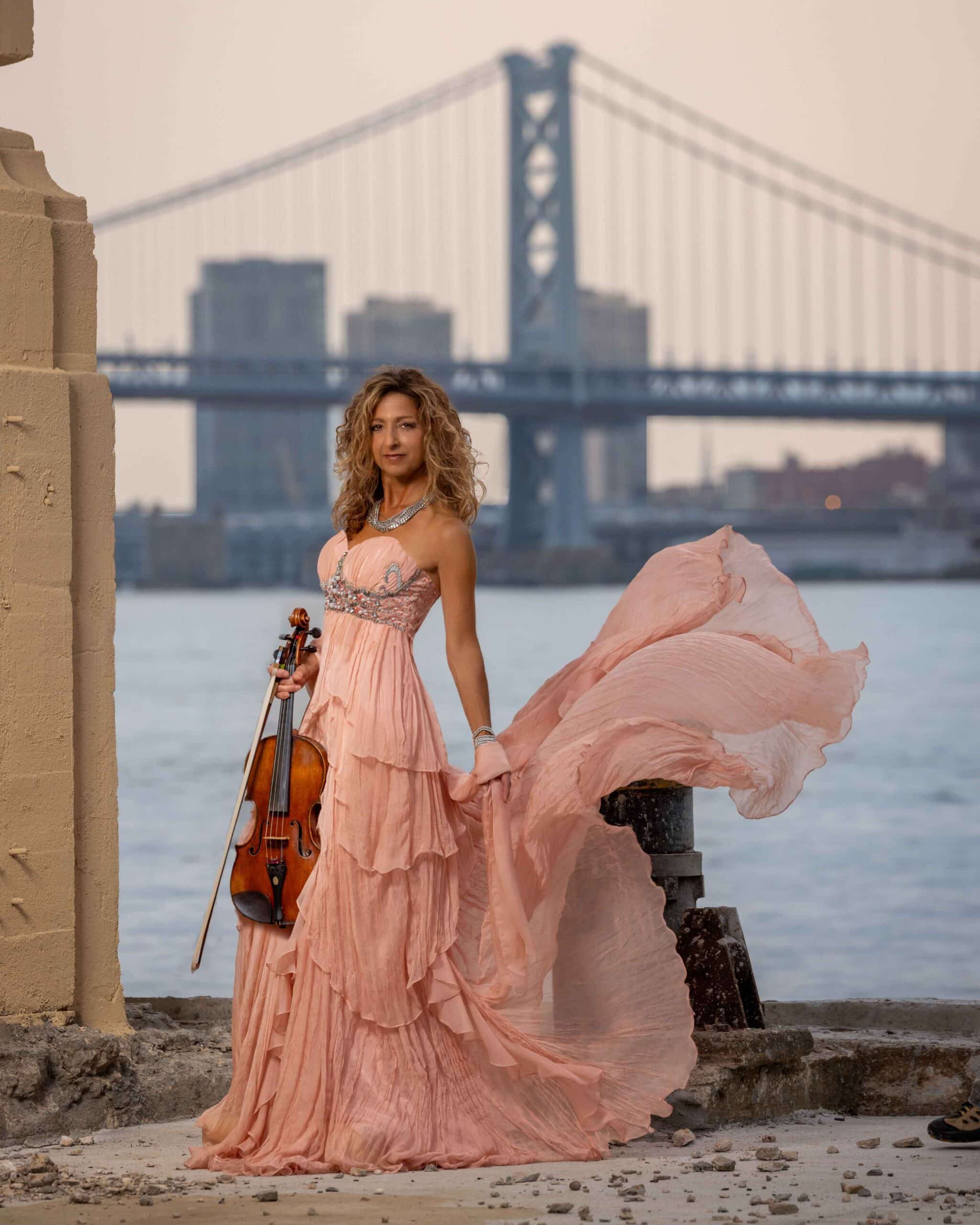 woman wearing a pink dress and holding a violin in an outdoor industrial setting
