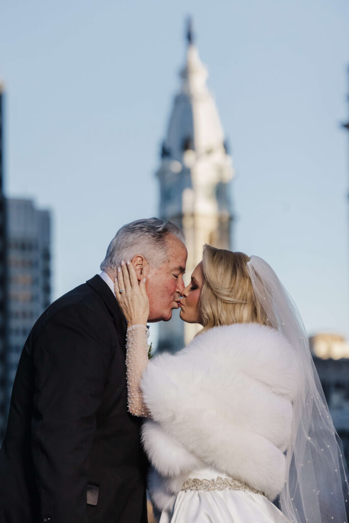 Bride and groom kissing with Philadelphia City Hall in the background during Logan Hotel wedding portraits