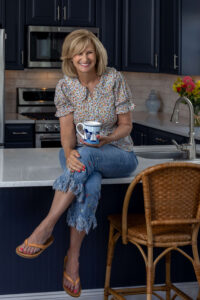 blonde woman laughing on kitchen counter while holding a blue and white coffee mug