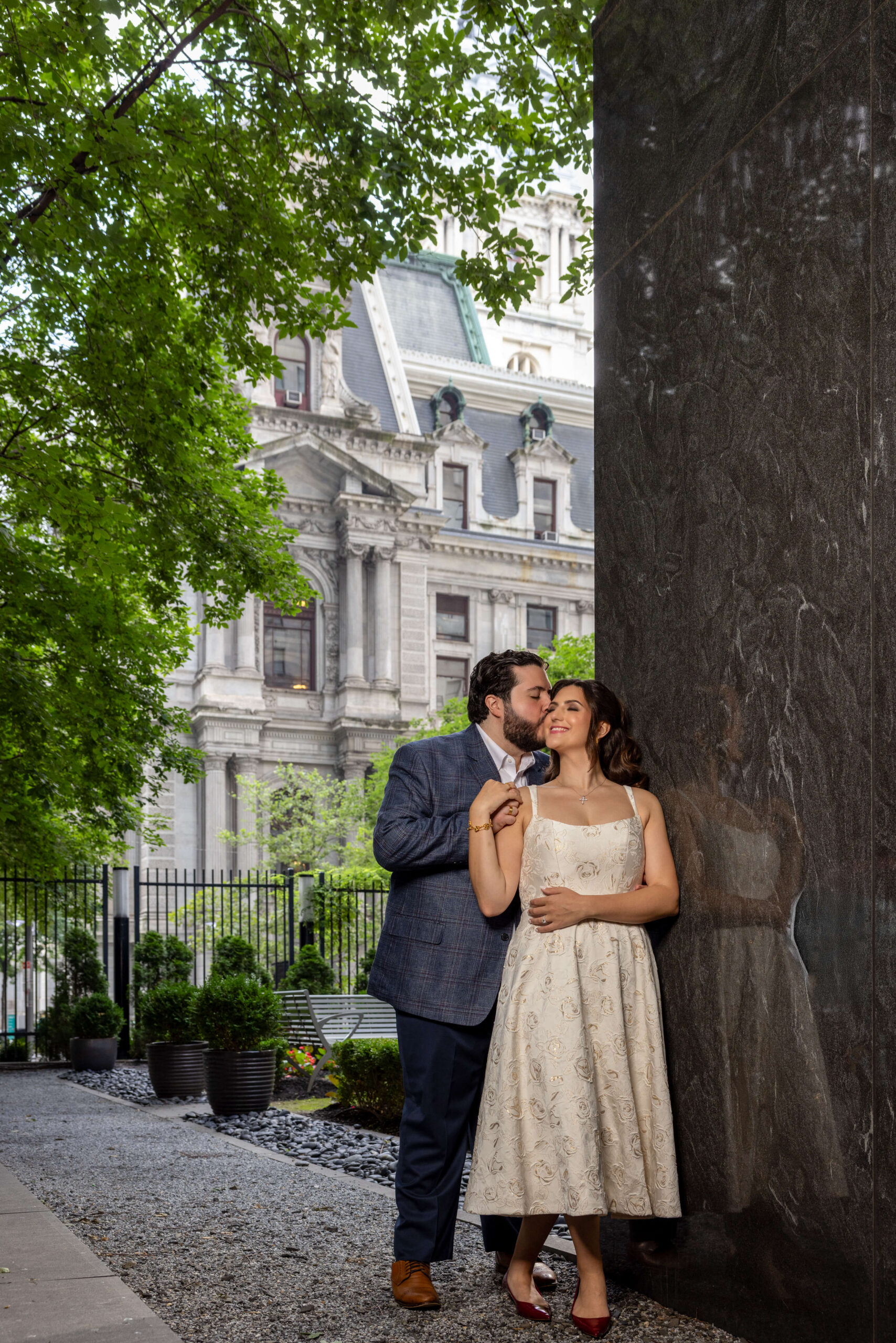 engaged couples kissing gently in the outdoor courtyard at the ritz carlton in philadelphia with city hall in the background