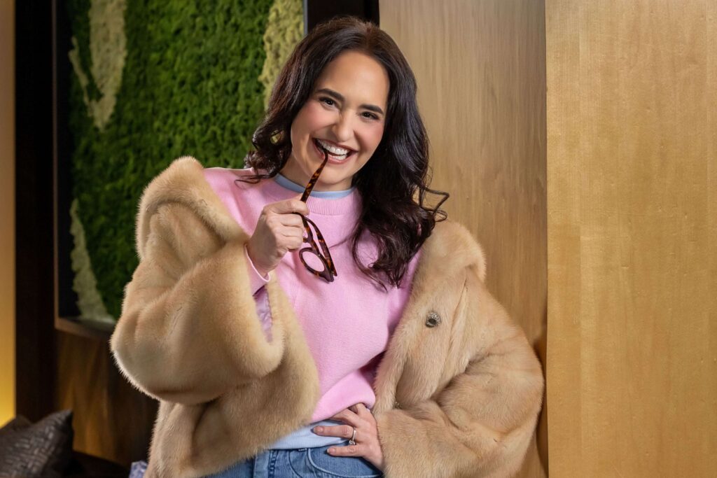 woman in a brown fur jacket and pink sweater biting glasses during editorial portrait photography session for a magazine. Photography by Phil Kramer