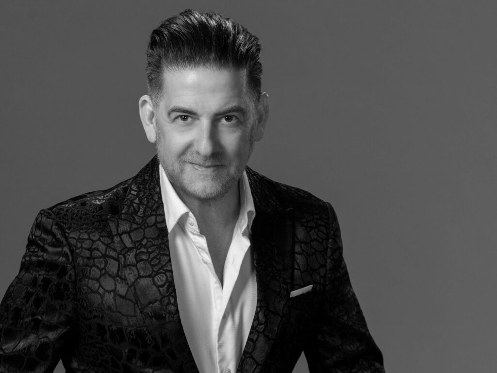 photo of phil kramer, a philadelphia commercial photographer, wearing a black alligator skin blazer and posing for a studio headshot with a slight smirk.