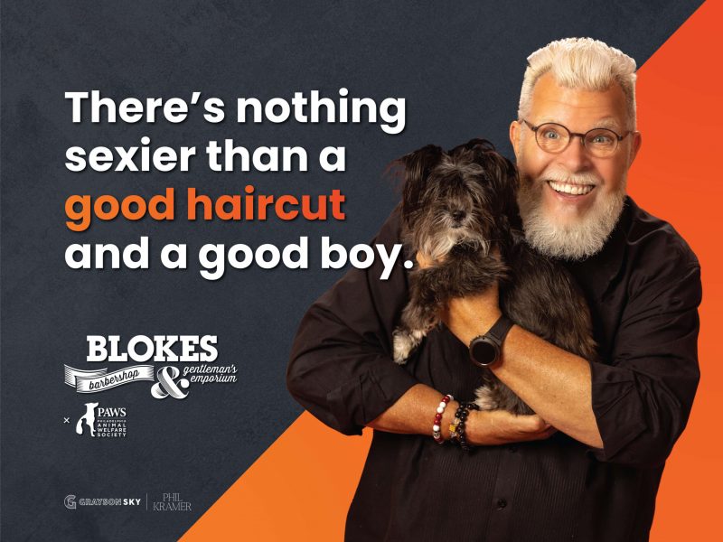 man with white hair smiling and holding a black dog