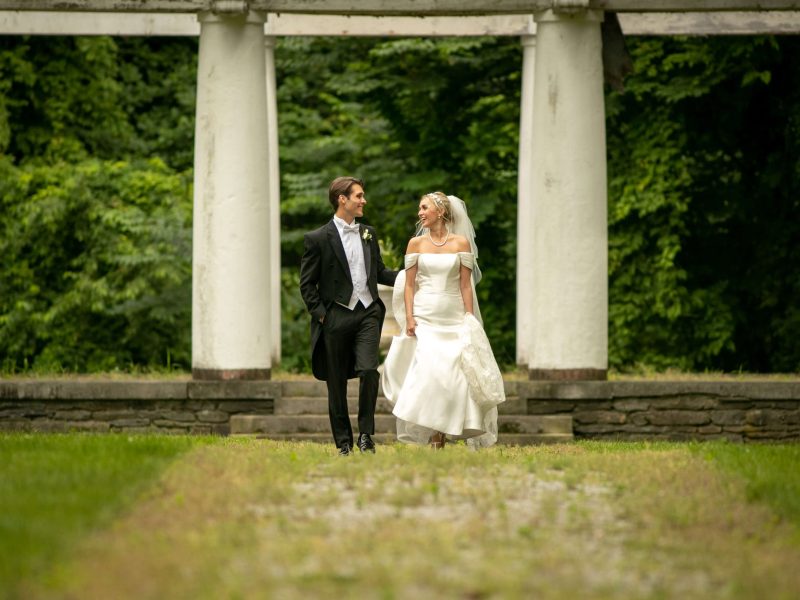 bride and groom walking by antique white columns in forest
