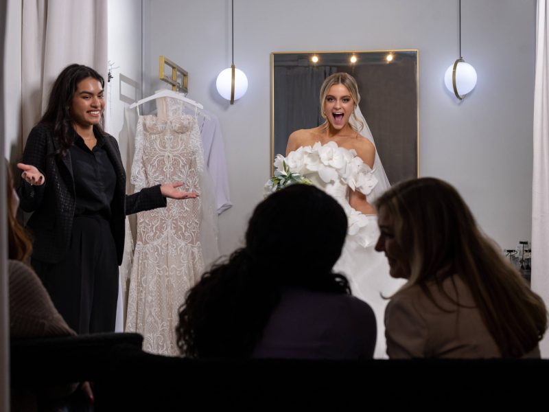 bride reveals wedding dress to family and friends from behind a dressing room curtain