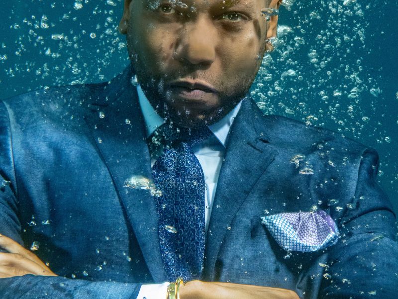 man crossing arms underwater in a luxury navy blue suit with a serious look on his face